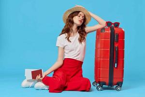 woman with red suitcase sitting on the floor blue background travel vacation photo