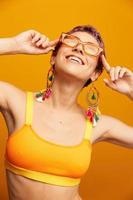 joven mujer en un brillante amarillo aptitud chandal con un abierto barriga y Gafas de sol en un naranja antecedentes sonriente foto