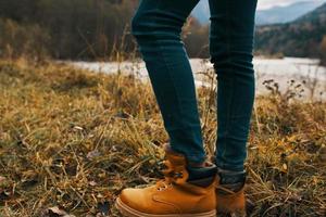 female legs in boots and jeans on nature in autumn in the mountains photo