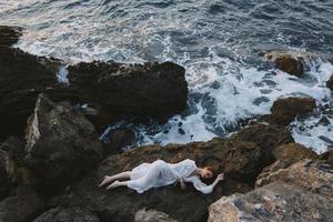 Beautiful bride lying on rocky coast with cracks on rocky surface view from above photo