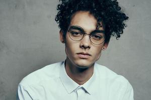 portrait of a nice guy with curly hair on a gray background and a light shirt glasses model close-up photo