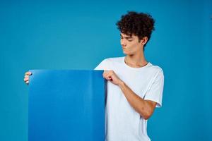 guy in a white t-shirt holding a poster mockup advertising blue background photo