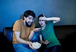 un hombre y un asustado mujer acecho un película en el noche en el sofá con un plato de palomitas de maíz foto