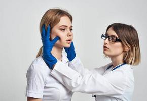 un mujer médico en un médico vestido y azul guantes examina el del paciente cara foto