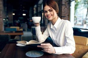 woman in skirt shirt at table in cafe coffee cup in hand and notepad pen photo