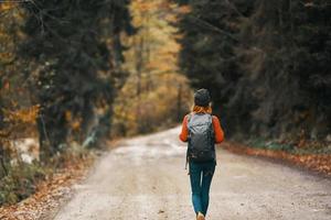 woman with backpack on the road in the forest in autumn landscape tall trees model photo