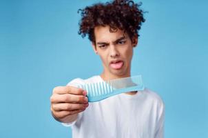 guy with curly hair holding a comb in front of his face on a blue background and disgust photo