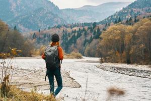 mujer en pantalones y un chaqueta con un mochila cerca el río en el montañas paisaje naturaleza foto