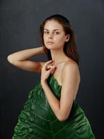 woman with bare shoulders hiding behind palm leaf charming look in dark background photo