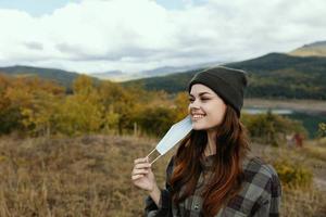 Happy woman with a medical mask in hands and mountains in the autumn background Trees photo