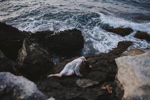 hermosa joven mujer en un blanco vestir acostado en un Roca en un blanco vestir paisaje foto