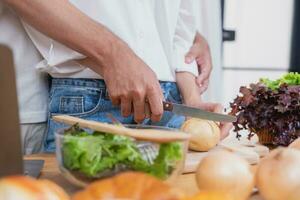 joven asiático Pareja Cocinando con frutas y vegetales y utilizando ordenador portátil en el cocina a cocinar comida juntos dentro el familia felizmente, familia concepto. foto