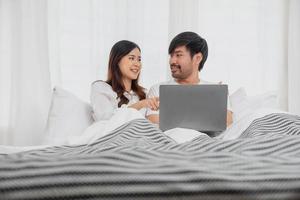 joven contento asiático Pareja utilizando ordenador portátil en cama acecho película, romántico hora a mejorar familia relación, familia concepto. foto