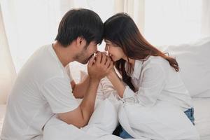 contento joven asiático Pareja abrazando, broma, jugando alegremente en cama a hogar, romántico hora a mejorar familia vinculación familia concepto. foto