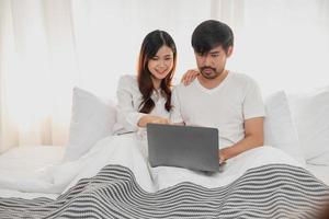 joven contento asiático Pareja utilizando ordenador portátil en cama acecho película, romántico hora a mejorar familia relación, familia concepto. foto