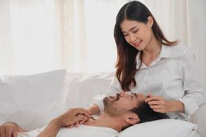 Happy young asian couple embracing, teasing, playing cheerfully in bed at home, romantic time to enhance family bonding. family concept. photo