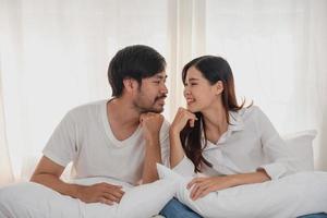 Happy young asian couple embracing, teasing, playing cheerfully in bed at home, romantic time to enhance family bonding. family concept. photo