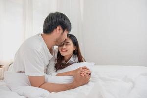 contento joven asiático Pareja abrazando, broma, jugando alegremente en cama a hogar, romántico hora a mejorar familia vinculación familia concepto. foto