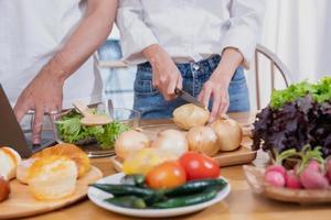 joven asiático Pareja Cocinando con frutas y vegetales y utilizando ordenador portátil en el cocina a cocinar comida juntos dentro el familia felizmente, familia concepto. foto