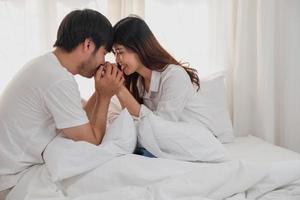 Happy young asian couple embracing, teasing, playing cheerfully in bed at home, romantic time to enhance family bonding. family concept. photo