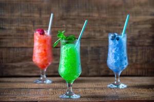 verano brillante postres de congelado arándano jugo, menta, Pepino y frambuesa jugo en vaso lentes con un Paja en un de madera antecedentes. verano Frío, tónico aplastada hielo cóctel, un tipo de sorbete foto