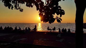 silhouetten van mensen zittend tegen de zon Aan de strand Bij zonsondergang video