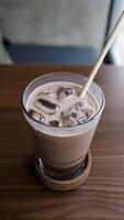 A glass of ice chocolate milk at a table with a straw. photo