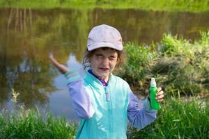 Girl sprays mosquito spray on the skin in nature that bite her hands and feet. Protection from insect bites, repellent safe for children. Outdoor recreation, against allergies. Summer time photo