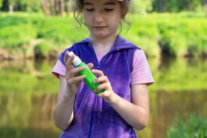 Girl sprays mosquito spray on the skin in nature that bite her hands and feet. Protection from insect bites, repellent safe for children. Outdoor recreation, against allergies. Summer time photo