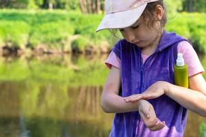 la chica rocía spray para mosquitos en la piel en la naturaleza que le muerde las manos y los pies. Protección contra picaduras de insectos, repelente seguro para niños. recreación al aire libre, contra las alergias. Hora de verano foto