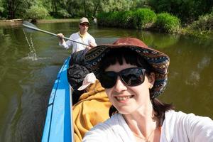 Man and woman couple, baby is sleeping, selfies are happy in family kayak trip rowing boat on the river, water hike, a summer adventure. Eco-friendly and extreme tourism, active and healthy lifestyle photo