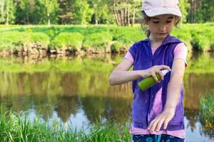 Girl sprays mosquito spray on the skin in nature that bite her hands and feet. Protection from insect bites, repellent safe for children. Outdoor recreation, against allergies. Summer time photo
