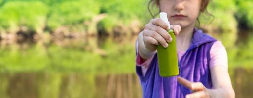 Girl sprays mosquito spray on the skin in nature that bite her hands and feet. Protection from insect bites, repellent safe for children. Outdoor recreation, against allergies. Summer time photo