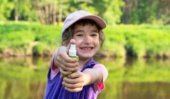 Girl sprays mosquito spray on the skin in nature that bite her hands and feet. Protection from insect bites, repellent safe for children. Outdoor recreation, against allergies. Summer time photo