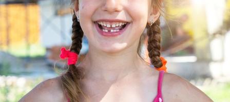 sin dientes contento sonrisa de un niña con un caído inferior Leche diente de cerca. cambiando dientes a molares en infancia foto