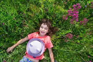 Portrait of a child in a hat with his face covered in summer lying in the grass and wildflowers. Hat with eyes and ears like a cat, summer time, freedom photo