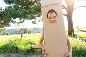 el niño es gracioso bailando y engañando alrededor en un caja disfraz - redondo separar para cara y manos. Moviente a un nuevo casa, para niños juegos desde improvisado medio, un traje con tu propio manos foto