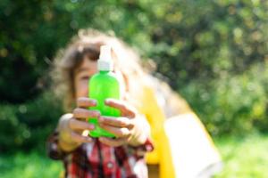 Girl uses a remedy for mosquitoes and biting insects in nature. Protection of skin from tick bites, gadflies, blood-sucking pests, means for children without allergens for outdoor camping. in defocus photo