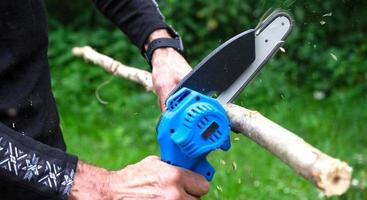 Hand-held portable camping electric saw on a battery for cutting firewood and wood. Close-up, a hand sawing a log, splinters flying photo