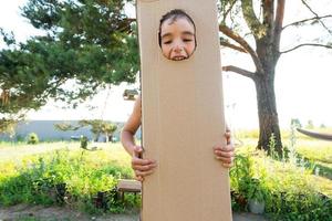 The child is funny dancing and fooling around in a box costume - round cutout for face and hands. Moving to a new house, children's games from improvised means, a suit with your own hands photo