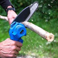 Hand-held portable camping electric saw on a battery for cutting firewood and wood. Close-up, a hand sawing a log, splinters flying photo