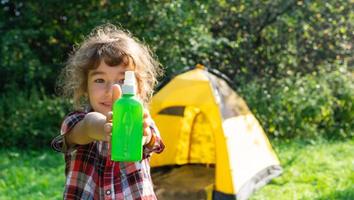 Girl sprays mosquito spray on the skin in nature that bite her hands and feet. Protection from insect bites, repellent safe for children. Outdoor recreation, against allergies. Summer time photo