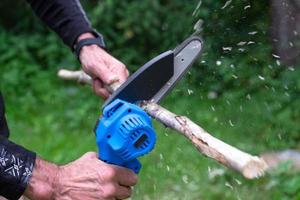 Hand-held portable camping electric saw on a battery for cutting firewood and wood. Close-up, a hand sawing a log, splinters flying photo