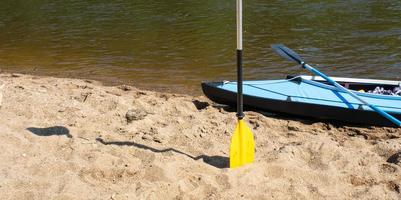 Tourist canoes with paddles stand on the river coast in summer on a water hike. Rafting on inflatable and frame double and triple kayak boats, family trip, extreme adventure in summer photo