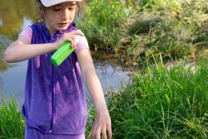 Girl sprays mosquito spray on the skin in nature that bite her hands and feet. Protection from insect bites, repellent safe for children. Outdoor recreation, against allergies. Summer time photo