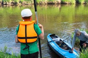 Child with a kayak paddle for rafting stands on the river bank. Family sport water hike, a summer adventure. Eco-friendly and extreme tourism, active and healthy lifestyle photo