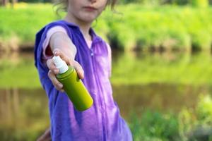 Girl sprays mosquito spray on the skin in nature that bite her hands and feet. Protection from insect bites, repellent safe for children. Outdoor recreation, against allergies. Summer time photo