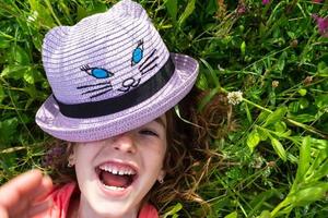Portrait of a child in a hat with his face covered in summer lying in the grass and wildflowers. Hat with eyes and ears like a cat, summer time, freedom photo