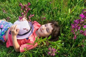 Portrait of a child in a hat with his face covered in summer lying in the grass and wildflowers. Hat with eyes and ears like a cat, summer time, freedom photo