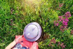 Portrait of a child in a hat with his face covered in summer lying in the grass and wildflowers. Hat with eyes and ears like a cat, summer time, freedom photo